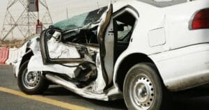 White car crushed in car accident. Side of the car is impacted and the driver's side door is pushed into vehicle, partially collapsed. 